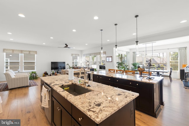 kitchen with sink, stainless steel dishwasher, light wood-type flooring, light stone countertops, and a spacious island