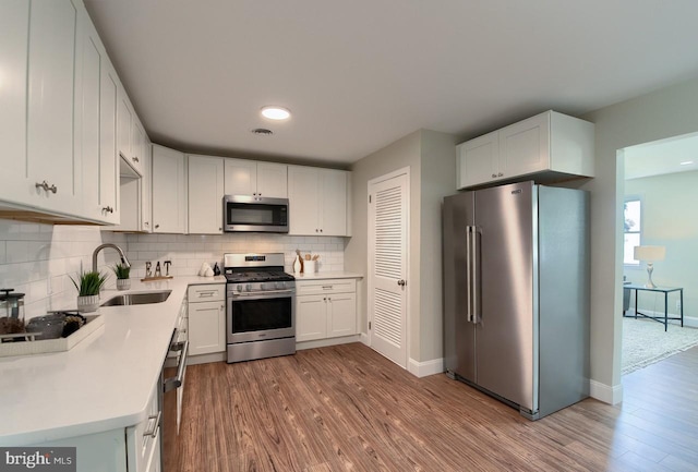 kitchen with appliances with stainless steel finishes, white cabinets, sink, backsplash, and hardwood / wood-style flooring