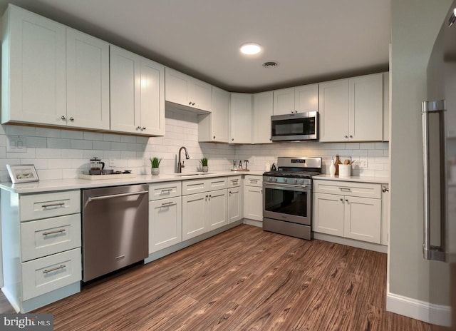 kitchen with white cabinets, dark hardwood / wood-style flooring, appliances with stainless steel finishes, decorative backsplash, and sink