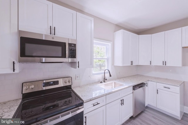 kitchen featuring light stone countertops, backsplash, stainless steel appliances, sink, and white cabinets