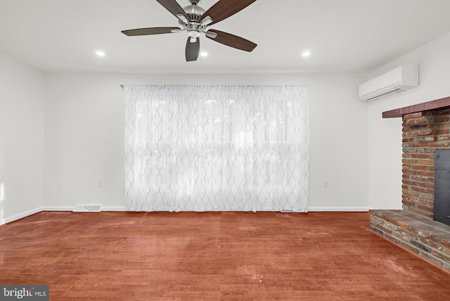 unfurnished living room with ceiling fan, wood-type flooring, a wall mounted AC, and a brick fireplace