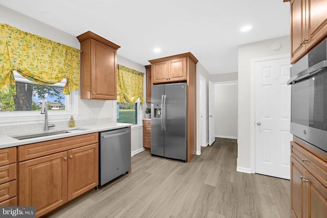 kitchen featuring sink, light wood-type flooring, light stone countertops, and appliances with stainless steel finishes