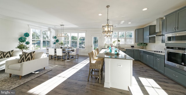 kitchen with wall chimney range hood, a wealth of natural light, decorative light fixtures, a kitchen island, and stainless steel appliances