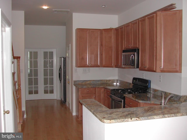 kitchen with light stone counters, kitchen peninsula, light wood-type flooring, and stainless steel appliances