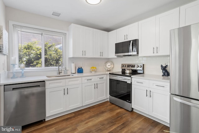 kitchen with sink, dark hardwood / wood-style floors, backsplash, white cabinets, and appliances with stainless steel finishes