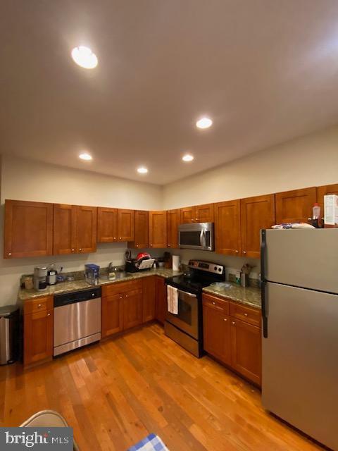 kitchen with appliances with stainless steel finishes, brown cabinetry, light wood-style flooring, and recessed lighting