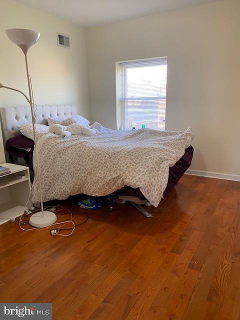 bedroom with wood finished floors, visible vents, and baseboards