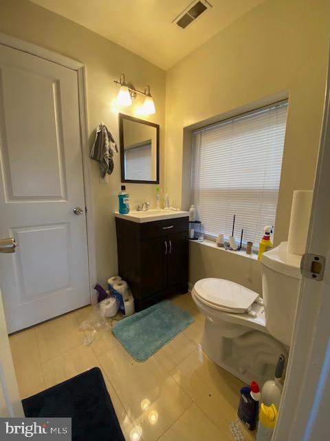 half bathroom with toilet, vanity, visible vents, and tile patterned floors