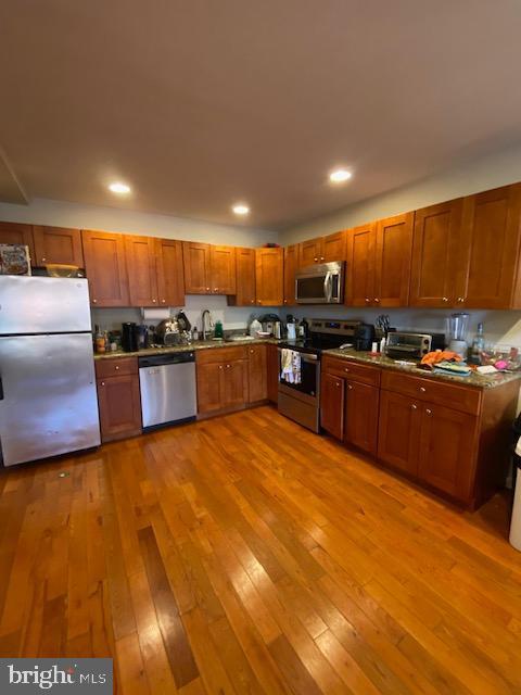 kitchen featuring brown cabinetry, light wood-style flooring, stainless steel appliances, a sink, and recessed lighting