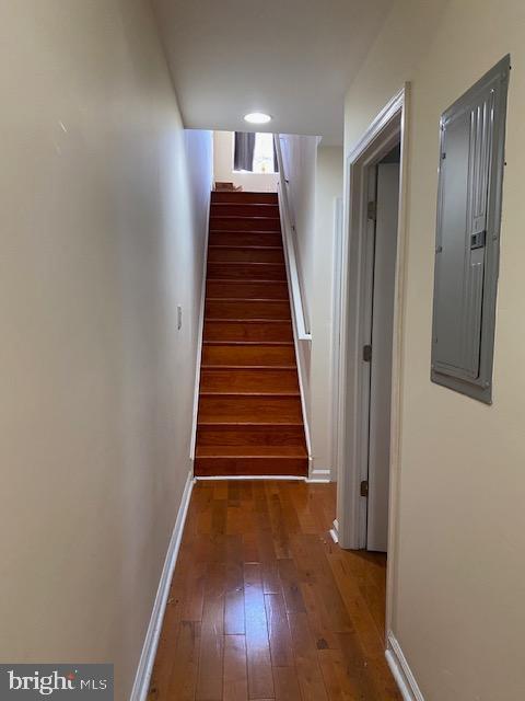 hall featuring stairs, electric panel, baseboards, and dark wood finished floors