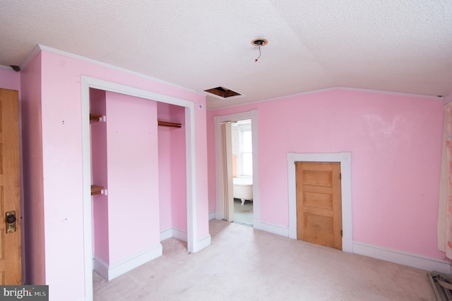 unfurnished bedroom featuring connected bathroom, a textured ceiling, a closet, light colored carpet, and vaulted ceiling