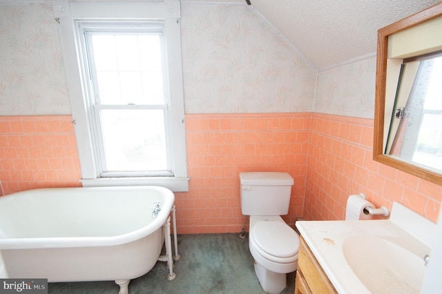 full bathroom featuring a wainscoted wall, toilet, a textured ceiling, a soaking tub, and wallpapered walls