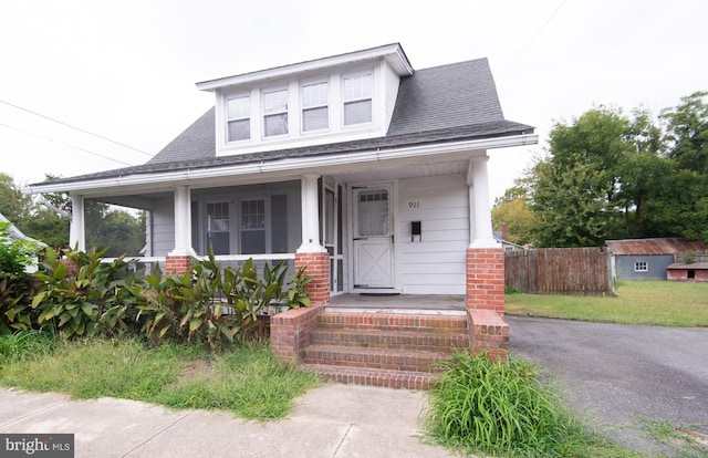 bungalow-style house with covered porch, a shingled roof, and fence