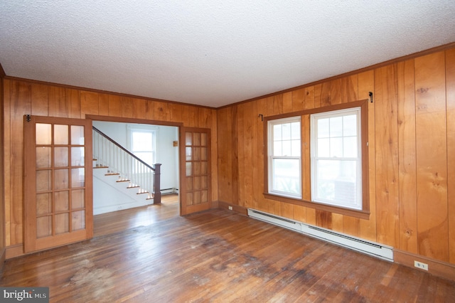 spare room featuring a baseboard radiator, wood walls, a textured ceiling, and dark hardwood / wood-style flooring