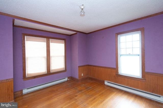 unfurnished room featuring a textured ceiling, wood-type flooring, crown molding, and a baseboard heating unit