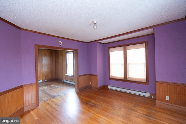 unfurnished room featuring wood-type flooring, a textured ceiling, baseboard heating, and crown molding