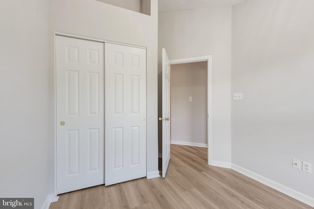 unfurnished bedroom with light wood-type flooring, a closet, and a towering ceiling