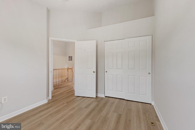 unfurnished bedroom featuring light wood-type flooring, a closet, and a high ceiling