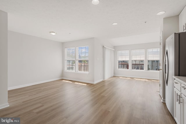 unfurnished living room with lofted ceiling, light wood-type flooring, and a textured ceiling