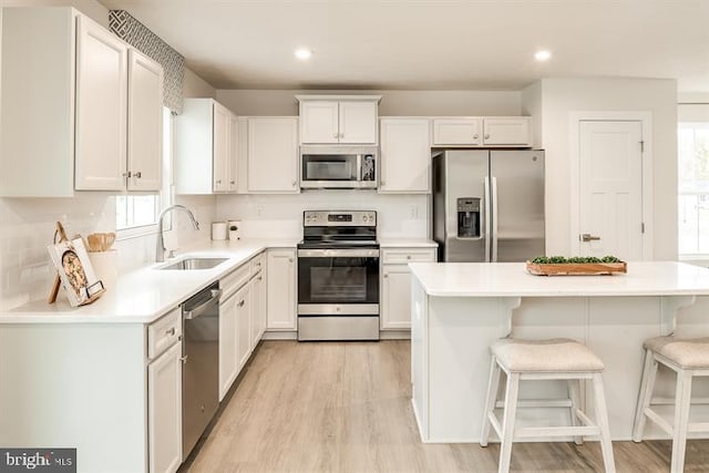 kitchen featuring sink, light hardwood / wood-style flooring, appliances with stainless steel finishes, white cabinets, and a kitchen bar