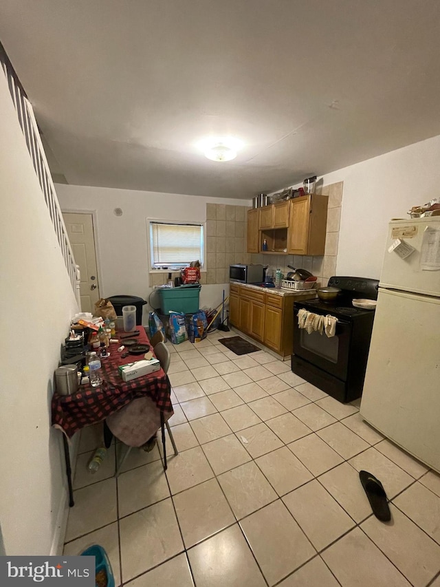 kitchen with white fridge, decorative backsplash, light tile patterned flooring, and black range with electric cooktop