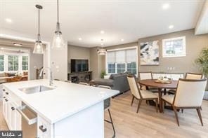 kitchen with a center island with sink, white cabinets, sink, hanging light fixtures, and light hardwood / wood-style flooring