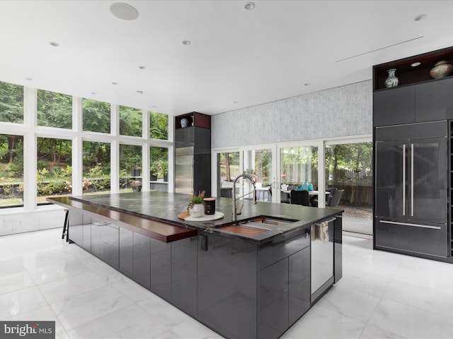 kitchen featuring sink, a large island with sink, paneled fridge, and a breakfast bar area