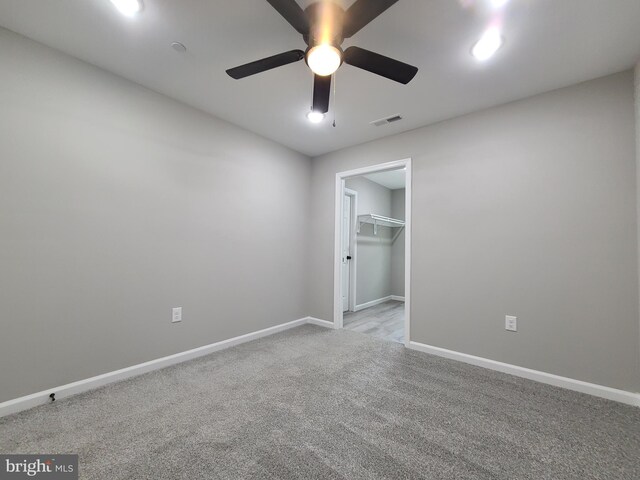 unfurnished bedroom featuring light carpet, a walk in closet, a closet, and ceiling fan