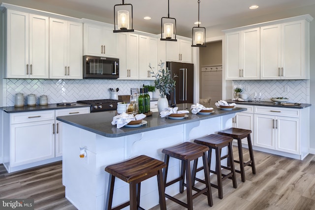 kitchen with tasteful backsplash, a center island, black appliances, hardwood / wood-style floors, and decorative light fixtures