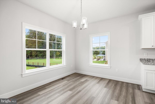 unfurnished dining area featuring a chandelier and light hardwood / wood-style flooring