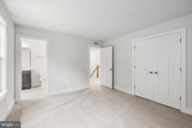 unfurnished bedroom featuring light carpet, a closet, and ensuite bath