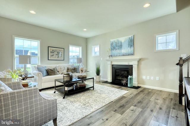 living room with recessed lighting, wood-type flooring, a fireplace with flush hearth, and baseboards