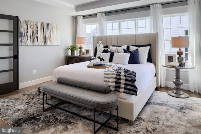 bedroom featuring a tray ceiling, crown molding, baseboards, and wood finished floors