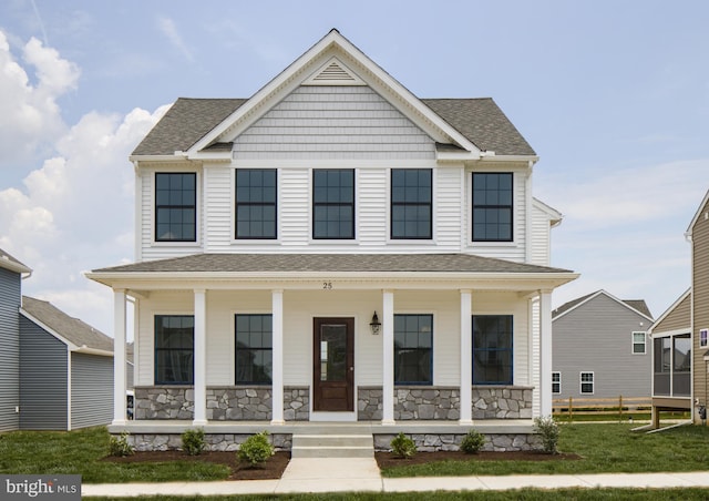 view of front of home featuring covered porch, a shingled roof, stone siding, and a front yard