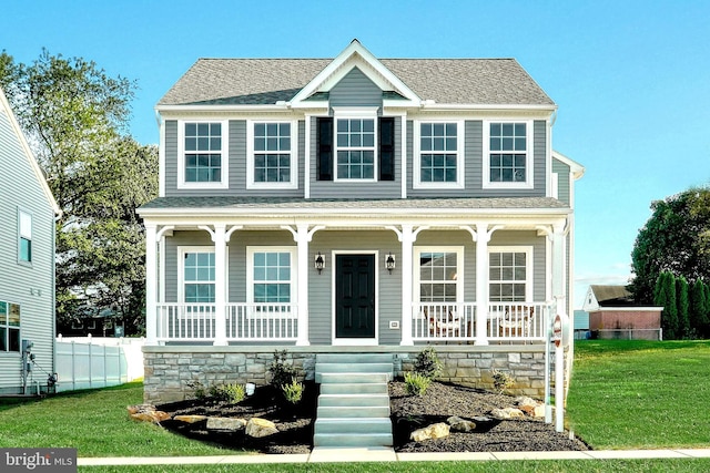 view of front facade with a shingled roof, a front yard, and covered porch