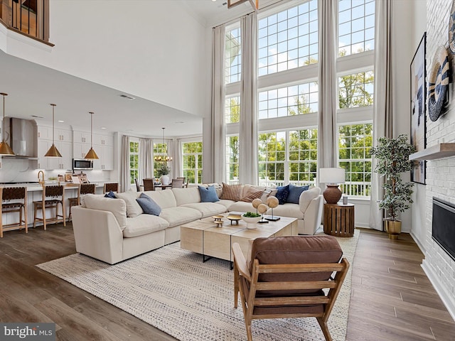 living room with a towering ceiling, a brick fireplace, plenty of natural light, and dark wood-type flooring