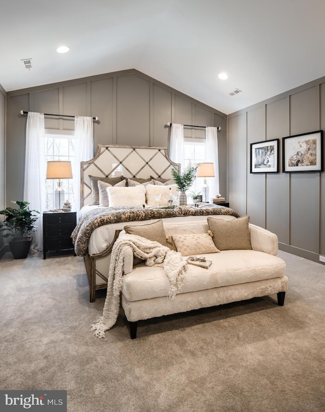 bedroom with light colored carpet, a decorative wall, visible vents, and vaulted ceiling