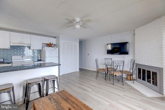 kitchen with light wood-type flooring, a brick fireplace, white cabinets, and white appliances