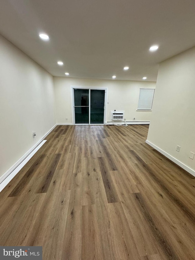 unfurnished living room featuring wood-type flooring, a baseboard radiator, and an AC wall unit