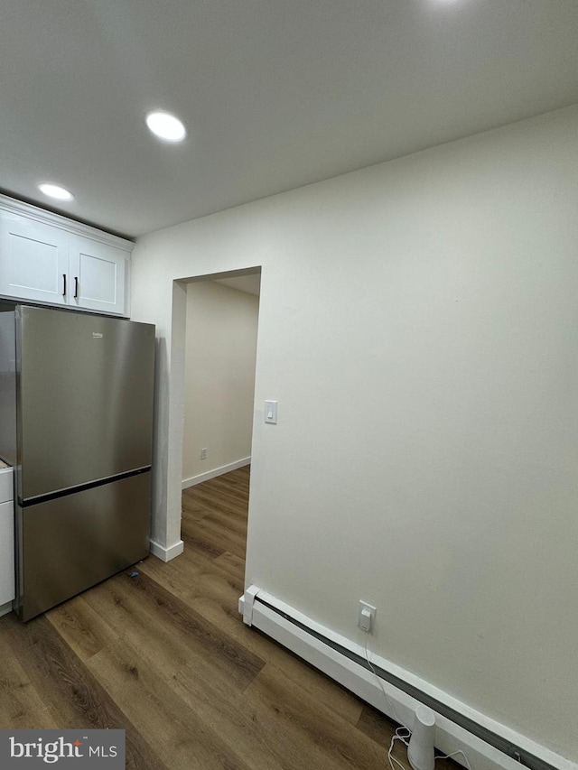 kitchen with wood-type flooring, white cabinetry, stainless steel refrigerator, and baseboard heating