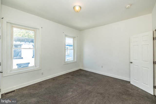 unfurnished room featuring dark colored carpet and a healthy amount of sunlight