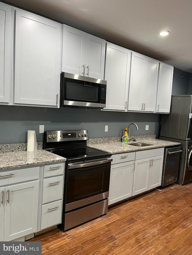 kitchen with light wood-type flooring, stainless steel appliances, sink, white cabinets, and stacked washer / drying machine