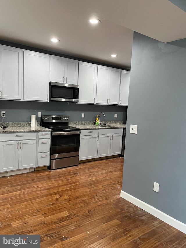 kitchen featuring sink, dark hardwood / wood-style flooring, light stone counters, white cabinetry, and stainless steel appliances