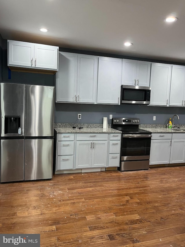 kitchen with light stone countertops, appliances with stainless steel finishes, light wood-type flooring, sink, and white cabinetry