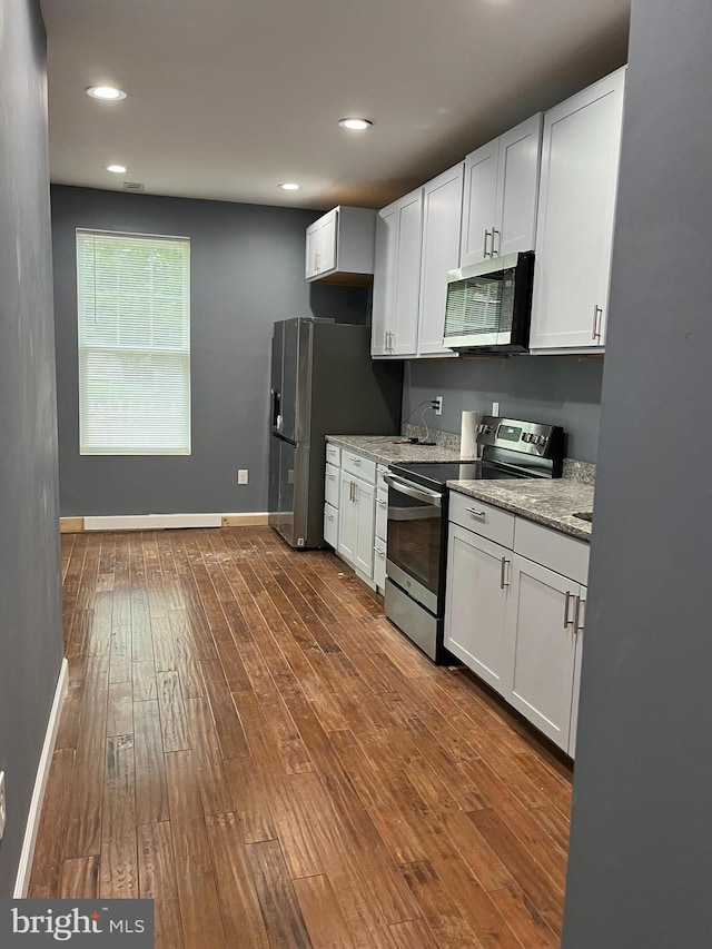 kitchen with white cabinets, dark hardwood / wood-style floors, light stone countertops, and stainless steel appliances