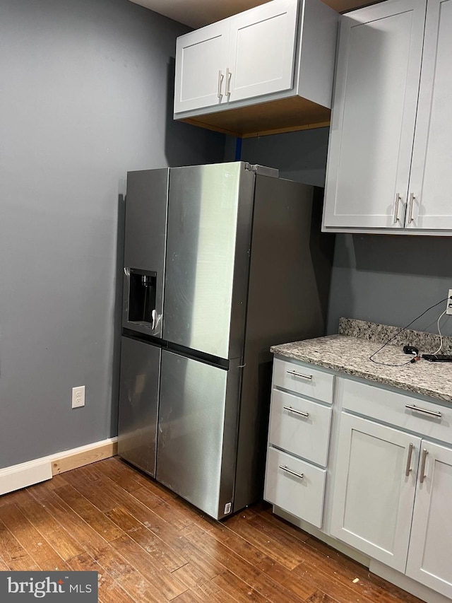 kitchen with stainless steel fridge, white cabinets, light stone counters, and wood-type flooring