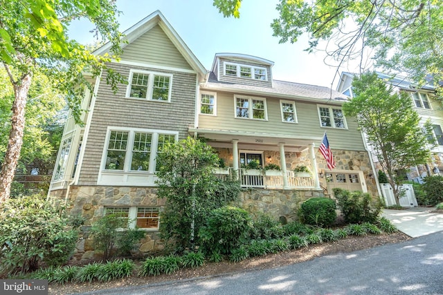 shingle-style home with a garage, stone siding, driveway, and fence