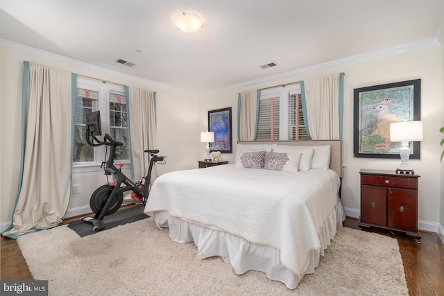 bedroom with ornamental molding, visible vents, baseboards, and wood finished floors