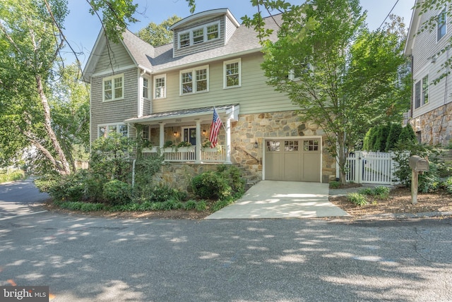 view of front of property with a shingled roof, concrete driveway, stone siding, an attached garage, and covered porch