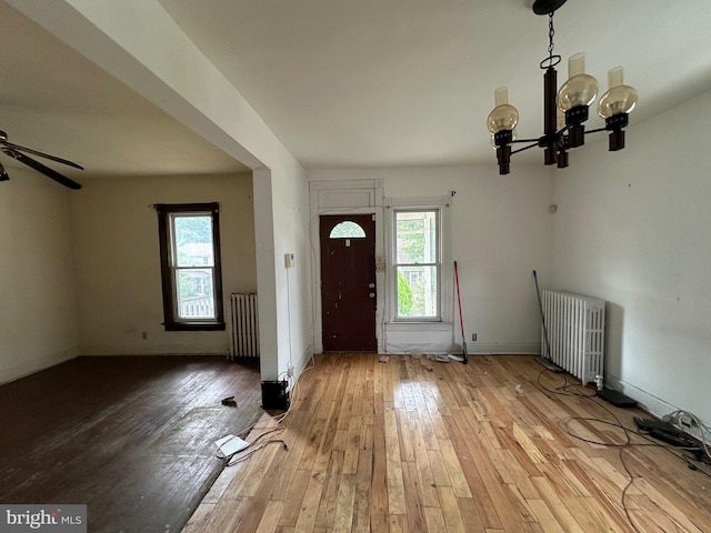 foyer with radiator, ceiling fan with notable chandelier, and light hardwood / wood-style flooring